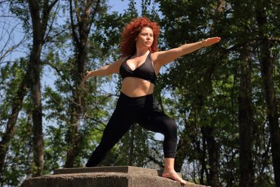 Redhead woman doing yoga against trees