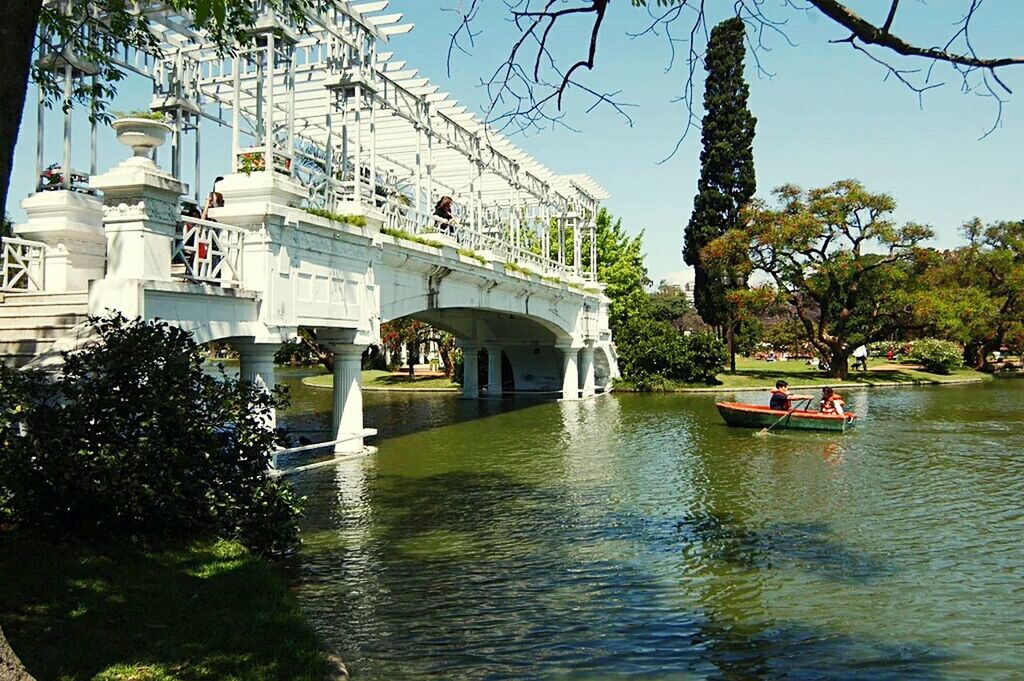 tree, water, architecture, built structure, building exterior, waterfront, nautical vessel, clear sky, incidental people, transportation, day, mode of transport, boat, river, sunlight, house, large group of people, canal, sky