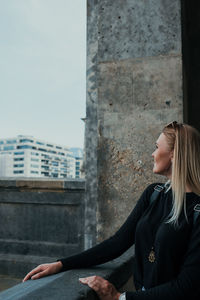 Side view of young woman sitting against building in city
