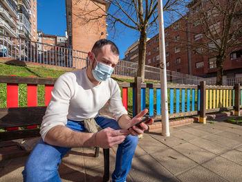 Full length of man sitting on mobile phone outdoors