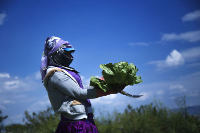 Woman standing by purple flower on field against sky