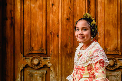 Portrait of smiling girl in traditional clothing standing against door