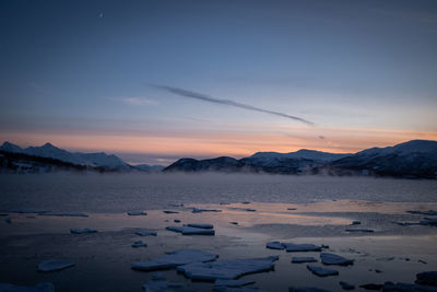 Icy bay winter panorama with scenic twilight sky behind mountains.
