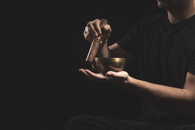 Detail of man sitting playing the tibetan singing bowl on black background with copyspace.