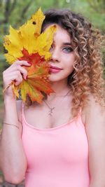 Portrait of beautiful young woman holding maple leaf standing outdoors