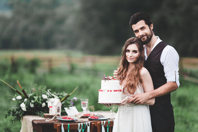 Portrait of smiling couple holding wedding cake at farm