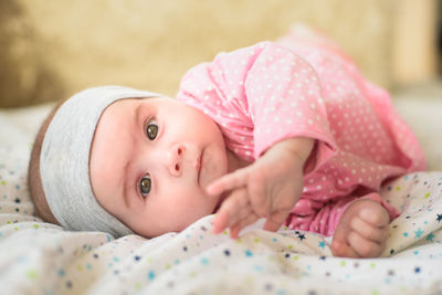 Portrait of cute baby girl lying on bed at home