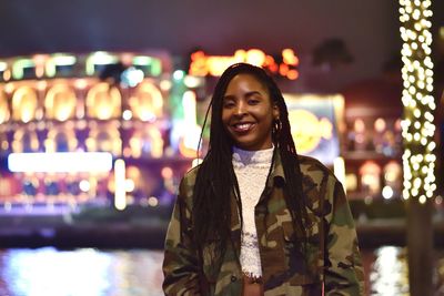 Portrait of woman smiling while standing in illuminated city at night