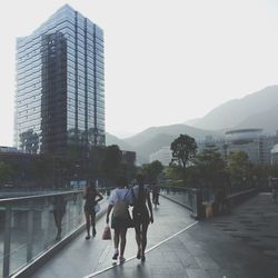 People walking on modern buildings in city against sky