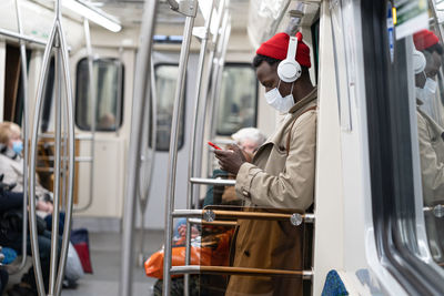 Side view of man wearing mask using mobile phone in train