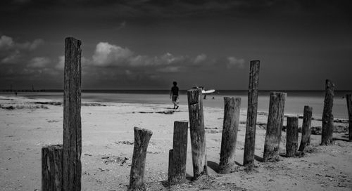 Man standing on wooden post on beach against sky