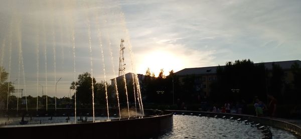 Fountain by building against sky during sunset