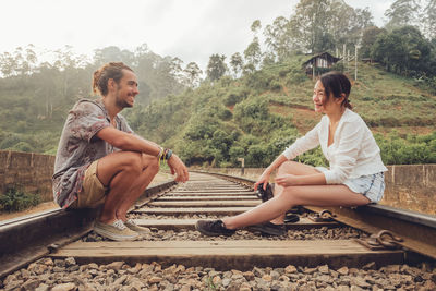 Friends sitting on railroad track against sky