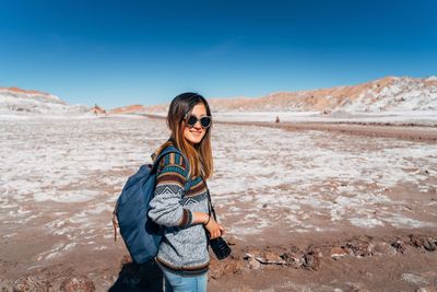 Portrait of young woman standing on desert against sky