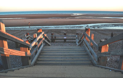 Staircase at beach against sky during sunset