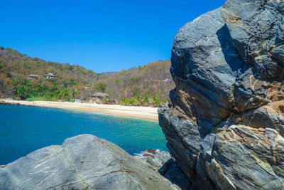 Rocks by sea against clear blue sky