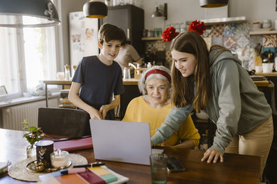 Girl using laptop with grandmother and brother at home