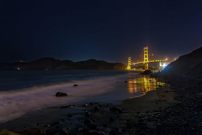 Illuminated city by sea against sky at night