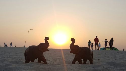 Elephant sculptures at sandy beach against sun during sunset