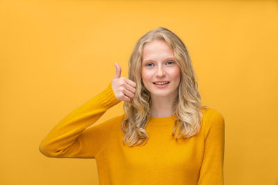 Portrait of smiling young woman against yellow background