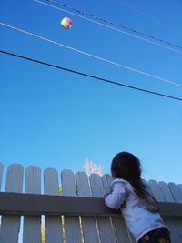 Low angle view of girl standing by fence while looking at ball