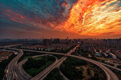 Multiple lane highway by cityscape against sky during sunset