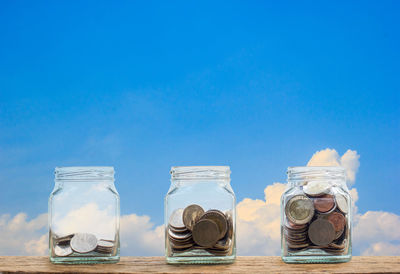 Close-up of coins in jar on table against sky