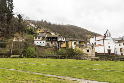 Houses on field by buildings against sky