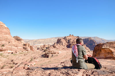 Full length of man sitting on rock against sky