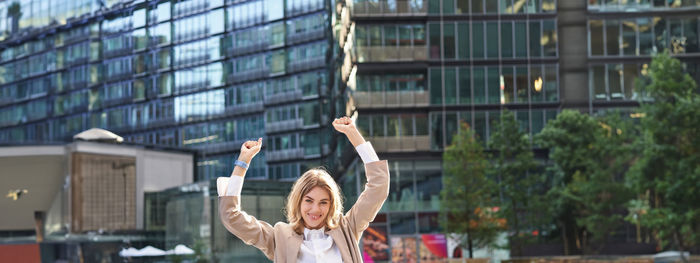 Rear view of woman with arms raised standing in city