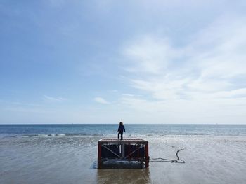 Rear view of boy on wooden structure at beach against sky