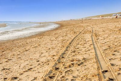 Tire tracks on beach against clear sky