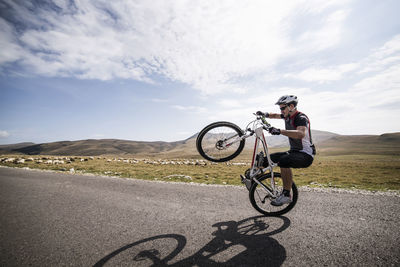 Man performing wheelie on road against sky