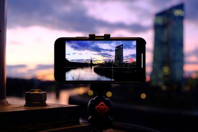 Mobile phone photographing river against sky during sunset