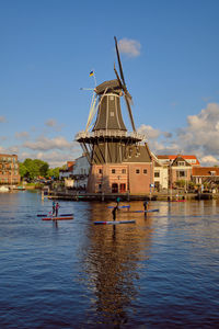 Sup paddleboarders passing the windmill on the river de spaarne in haarlem on a clear day.