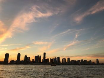 Modern cityscape by sea against sky during sunset