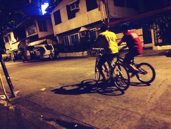 People riding bicycle on street against buildings at night