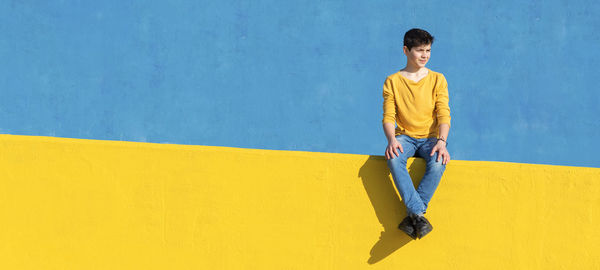 Portrait of boy sitting on yellow railing against blue wall