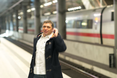 Portrait of man talking on mobile phone while standing at railroad station platform