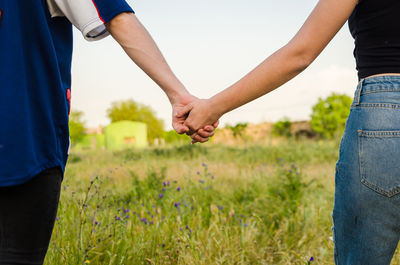 Midsection of couple holding hands on field