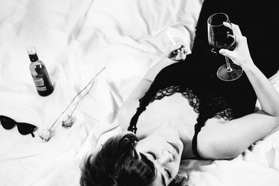 Woman smoking cigarette while having red wine on bed at home