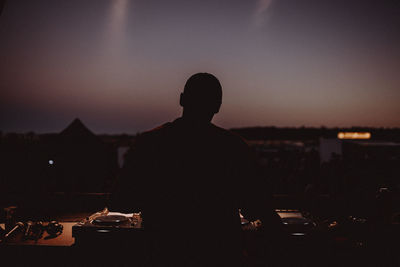 Rear view of silhouette man standing in city against sky during sunset