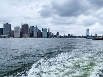 Sea by buildings in city against sky