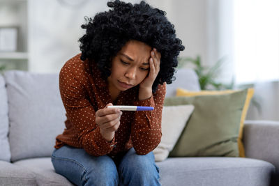 Young woman using phone while sitting on sofa at home