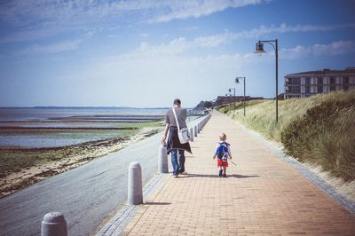 Rear view of father and son walking on footpath against sky