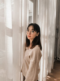 Portrait of young woman standing against curtain