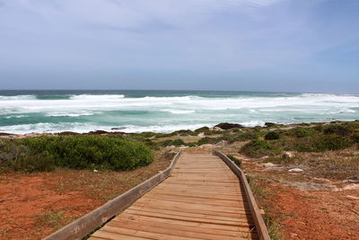 Boardwalk leading towards sea against sky