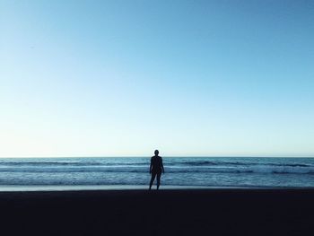 Full length of silhouette woman standing at beach against clear sky