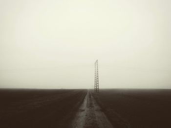 Electricity pylon on road against clear sky