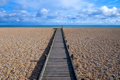 Boardwalk leading towards sea against sky